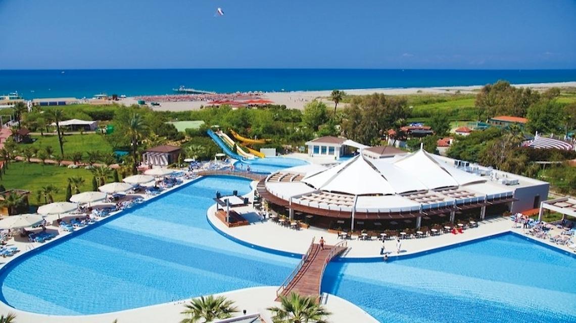 Außenansicht des Sunis Elita Beach Resort Hotel & Spa mit großem Pool, Sonnenliegen und Wasserrutschen.