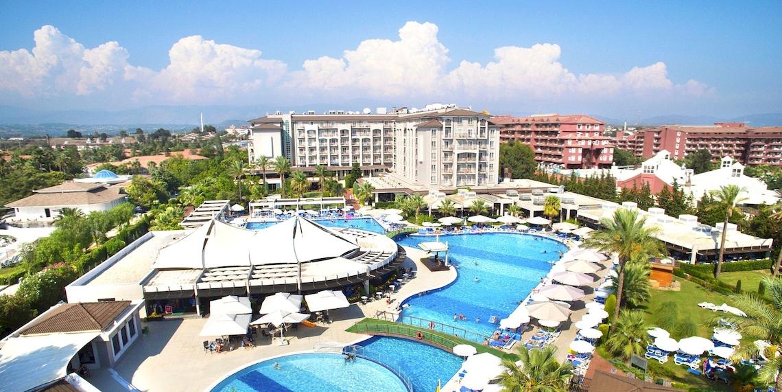 Luftaufnahme des Sunis Elita Beach Resort Hotels & Spa mit großen Swimmingpools und Sonnenschirmen.
