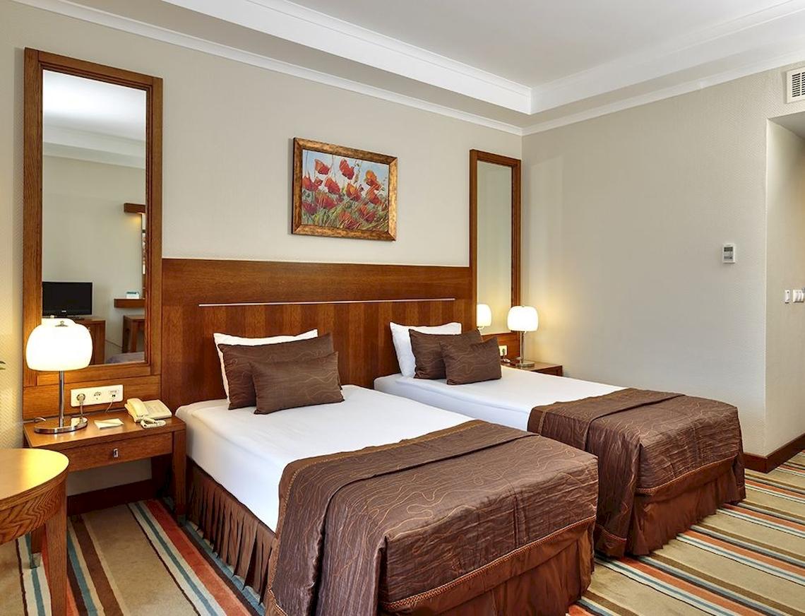 Zwei Doppelbetten in einem eleganten Hotelzimmer mit Spiegel und Kunstwerk.