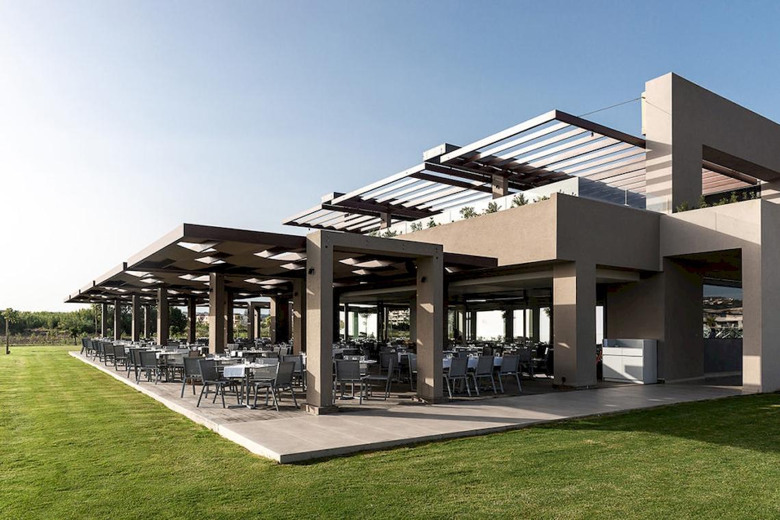 Außenbereich des Euphoria Resorts mit überdachten Tischen und Stühlen vor einer grünen Wiese.