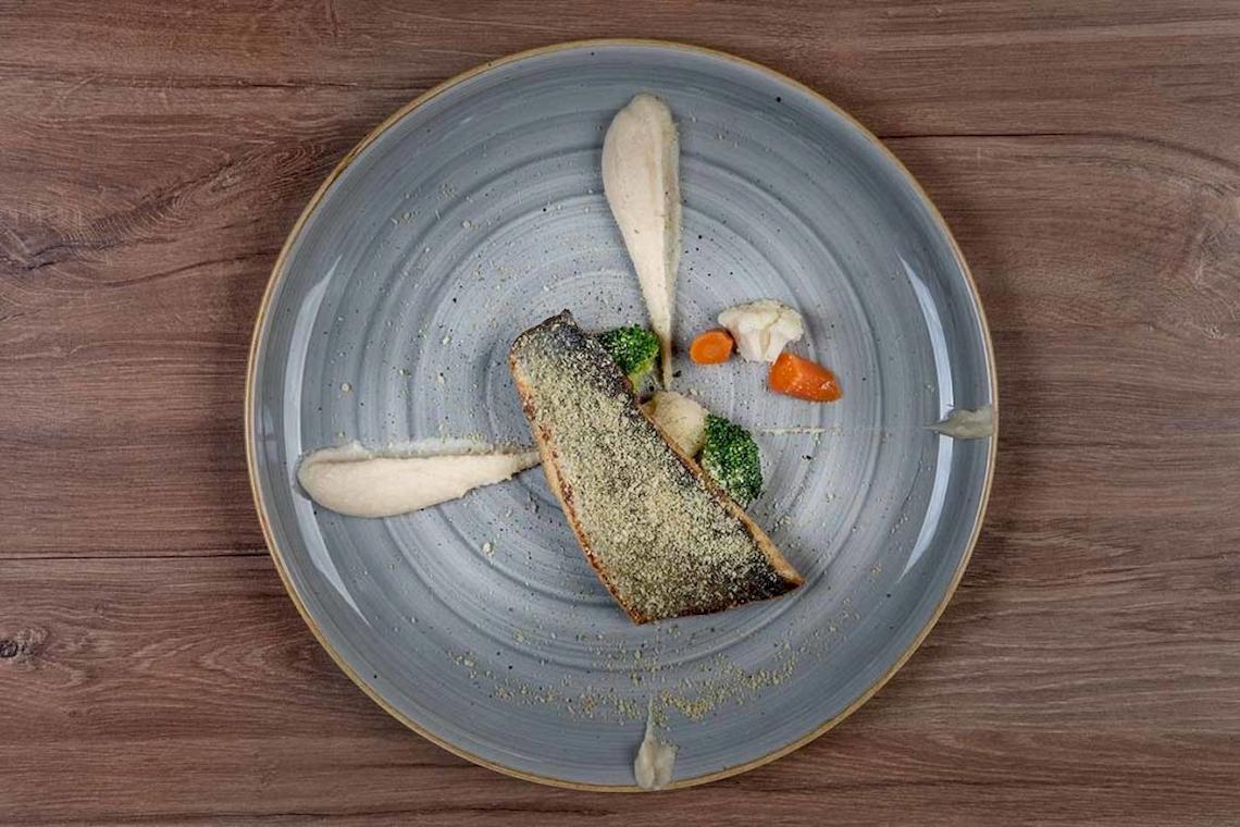 Teller mit Fisch und Gemüse auf einer Holzoberfläche.