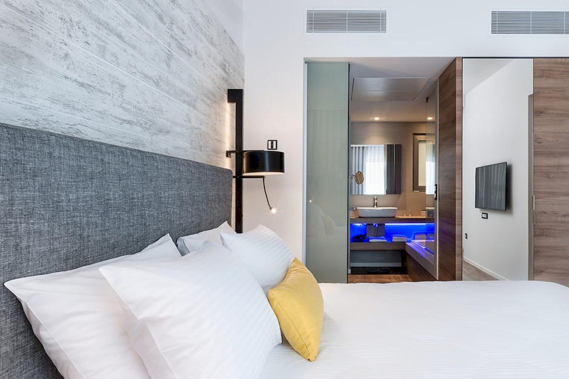 Schlafzimmer im Euphoria Resort mit Bett, Kissen, Lampe und Badezimmeransicht.
