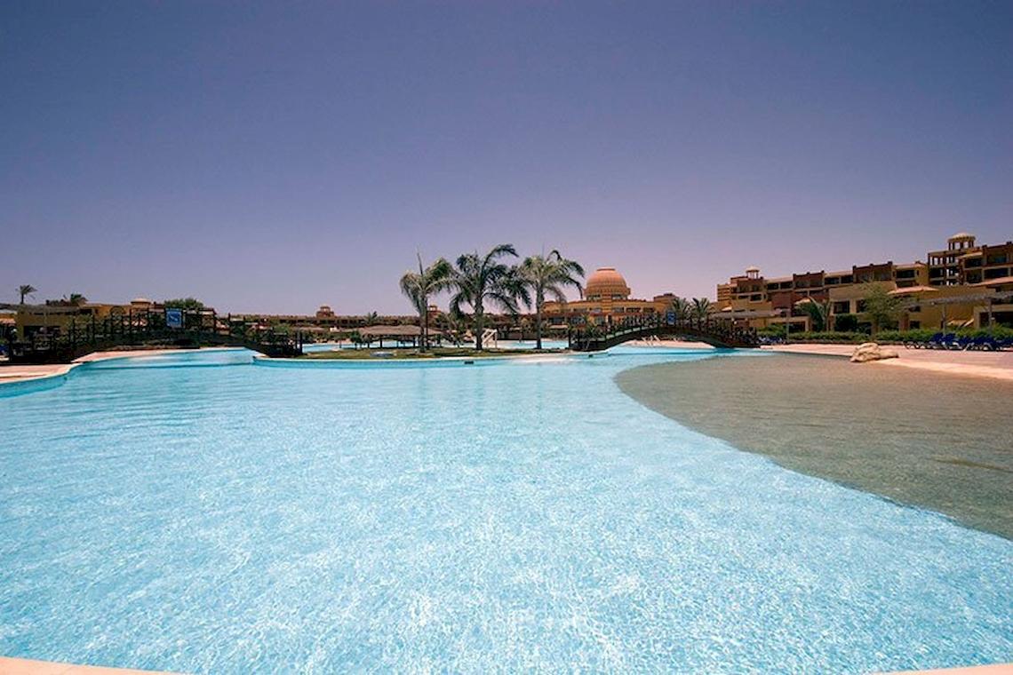 Ein großer Swimmingpool im Malikia Resort Abu Dabbab mit einer Brücke und Palmen im Hintergrund.