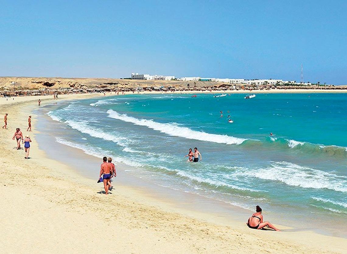 Besucher genießen den Strand am Malikia Resort Abu Dabbab mit kristallklarem Wasser und blauem Himmel.