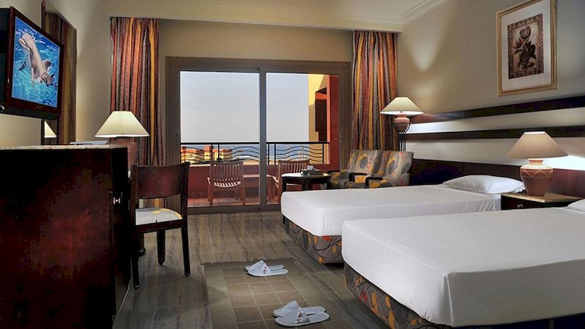 Doppelzimmer im Malikia Resort Abu Dabbab mit zwei Betten, Fernseher, Schreibtisch und Balkon mit Meerblick.