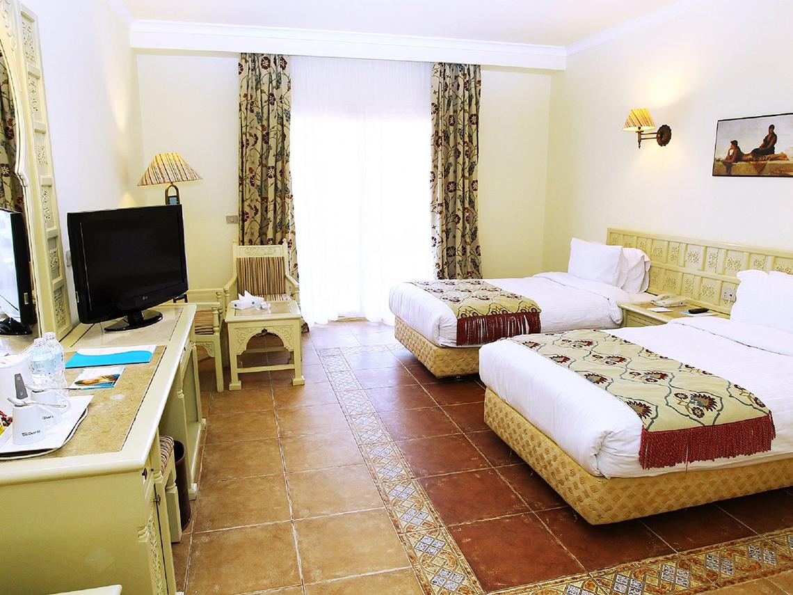 Zwei Betten in einem Hotelzimmer des Sentido Mamlouk Palace mit Fernseher, Lampen und Dekor.