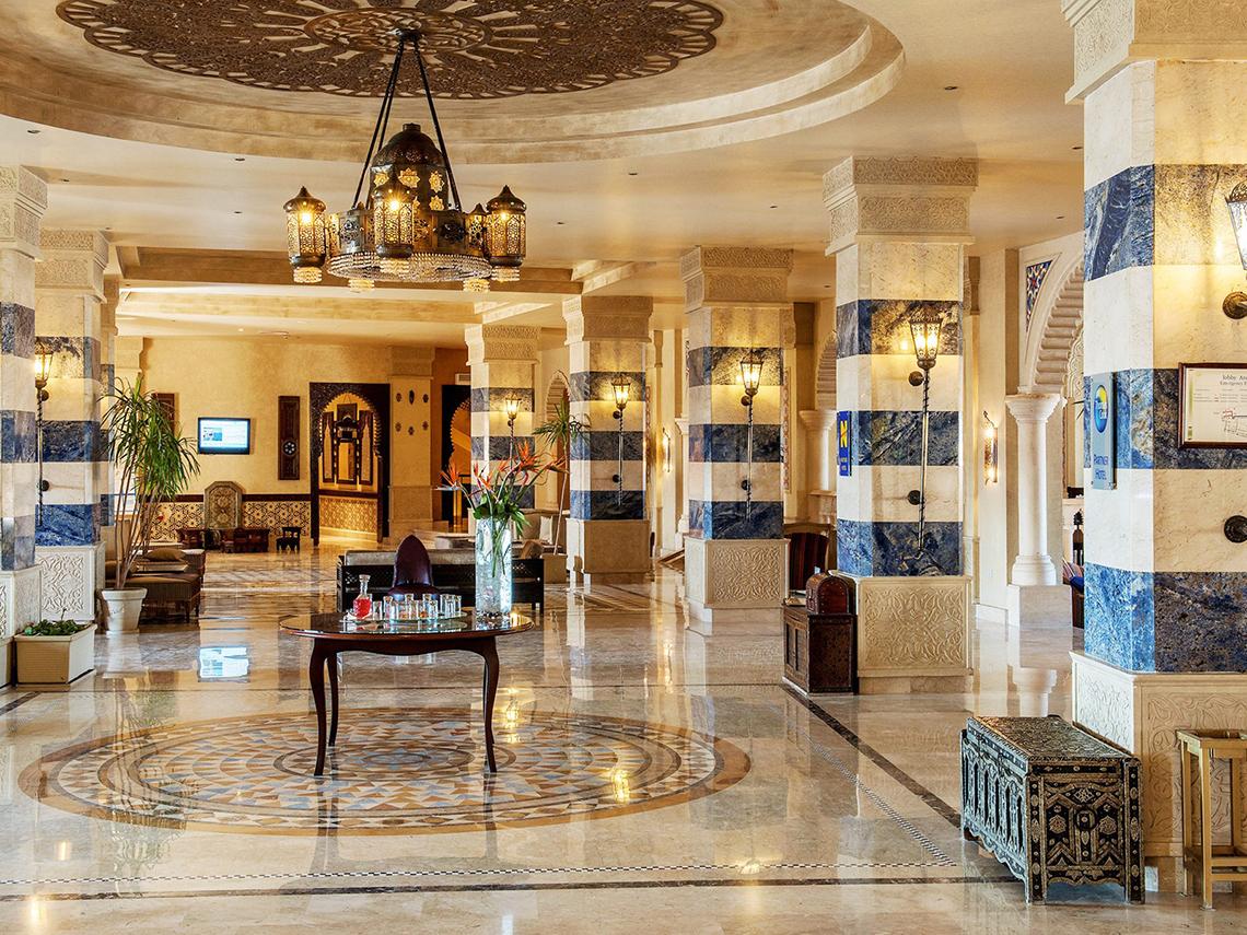 Das Hotelfoyer von Sentido Mamlouk Palace mit Säulen, einem Kronleuchter und einer zentralen Tischdekoration.