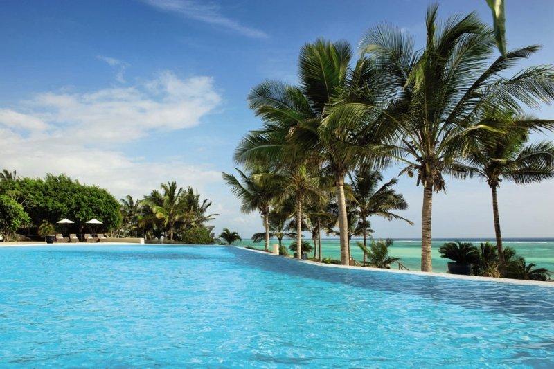 Ein großer Pool am Melia Zanzibar Hotel mit Palmen und Blick auf das Meer.