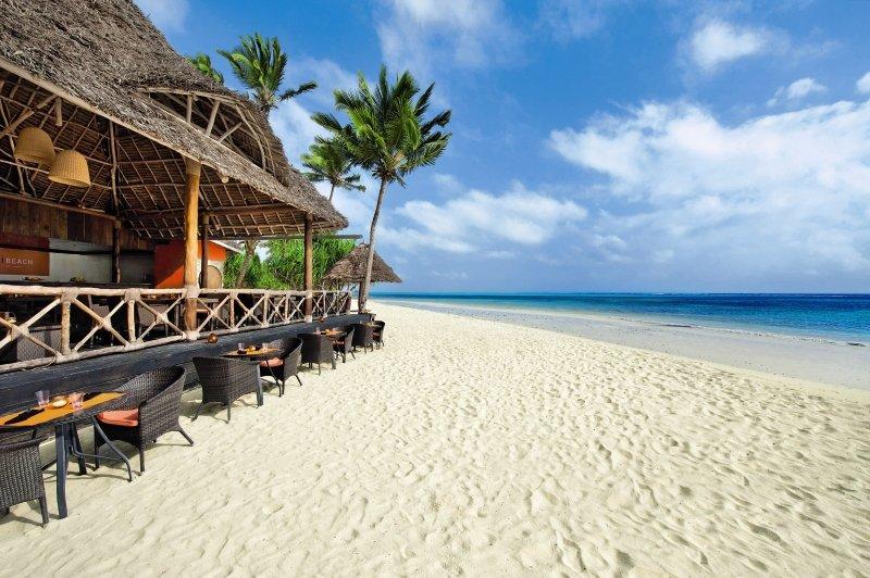 Strand und Restaurant des Melia Zanzibar Hotels mit Palmen und Tischen im Freien