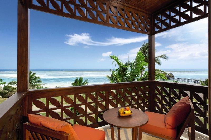 Balkon des Melia Zanzibar Hotels mit Blick auf das Meer und zwei roten Stühlen mit Kissen.