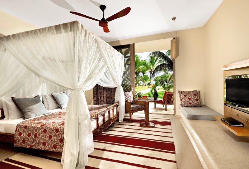 Schlafzimmer im Melia Zanzibar Hotel mit Himmelbett, Fernseher und Aussicht auf Palmen.