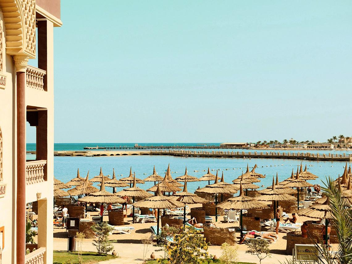 Strandansicht des Sentido Mamlouk Palace Hotels mit vielen Sonnenschirmen und Gästen.