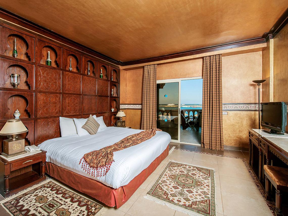 Innenansicht eines Schlafzimmers im Sentido Mamlouk Palace Hotel mit großem Bett, Nachttischen und Meerblick.