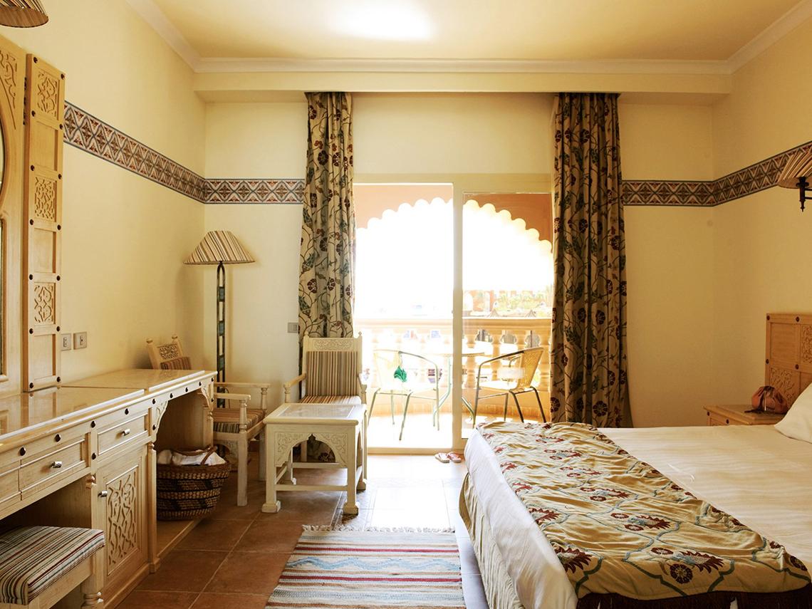 Ein Hotelzimmer im Sentido Mamlouk Palace mit einem Bett, Schreibtisch, Stühlen und einem Balkon.