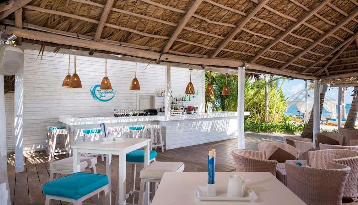 Strandbar des Catalonia Royal Bavaro Hotels mit weißen Tischen, blauen Stühlen und Blick auf das Meer.