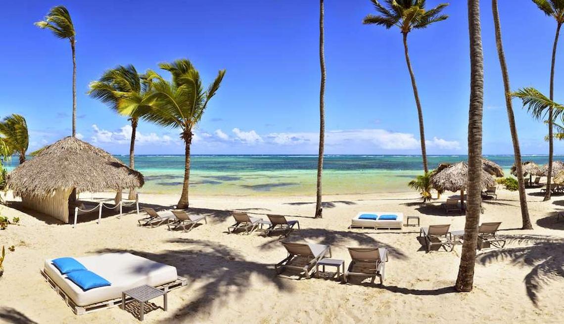 Strand des Catalonia Royal Bavaro Hotels mit weißen Liegen, Palmen und blauem Himmel