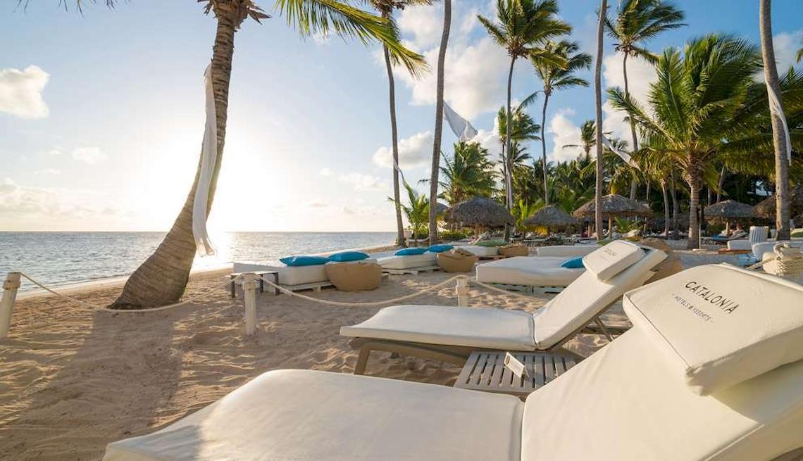 Sonnenaufgang am Strand des Catalonia Royal Bavaro mit weißen Liegen, Palmen und blauem Himmel.