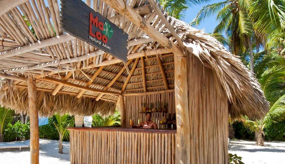 Strandbar mit Palmenhut und Frau an der Theke, serviert Cocktails und frische Säfte.