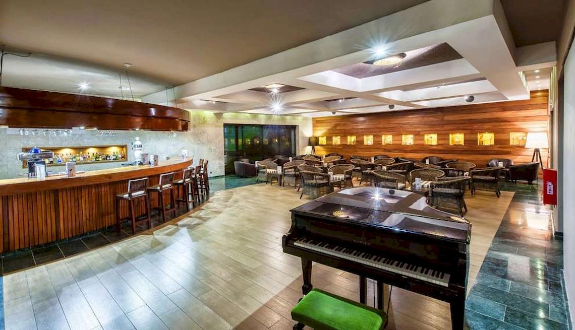 Innenbereich des Hotels Catalonia Royal Bavaro mit Bar, Klavier und runden Tischen.