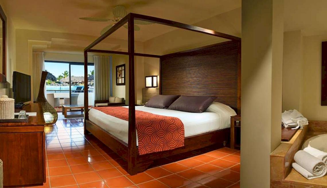 Innenansicht eines Hotelzimmers im Catalonia Royal Bavaro mit einem Himmelbett, einem Fernseher und einem Ausblick auf den Pool.