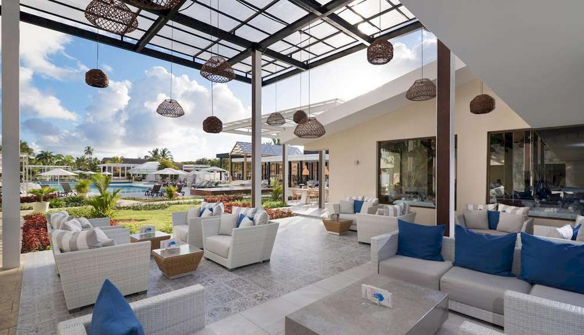 Loungebereich im Catalonia Royal Bavaro Hotel mit weißen Möbeln, blauen Kissen und einer Aussicht auf einen Pool.