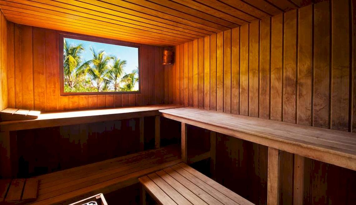 Innenansicht einer Sauna im Catalonia Royal Bavaro mit Holzwänden, Fenster und Palmen draußen.
