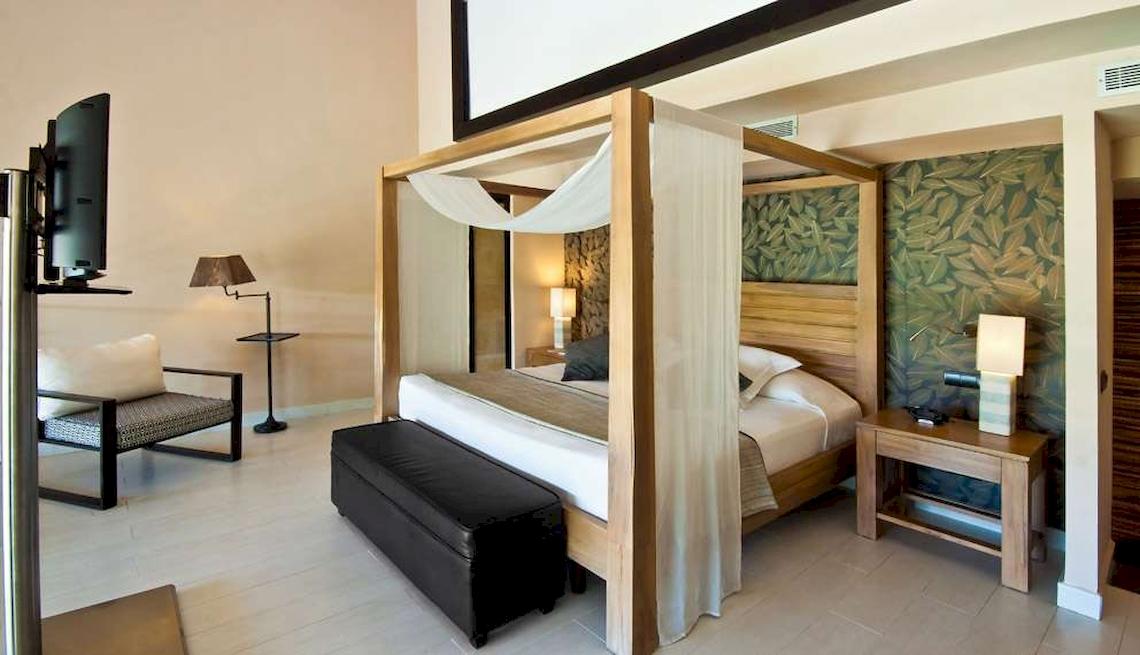 Hotelzimmer im Catalonia Royal Bavaro mit Himmelbett, Fernseher, Lampe und Nachttisch.