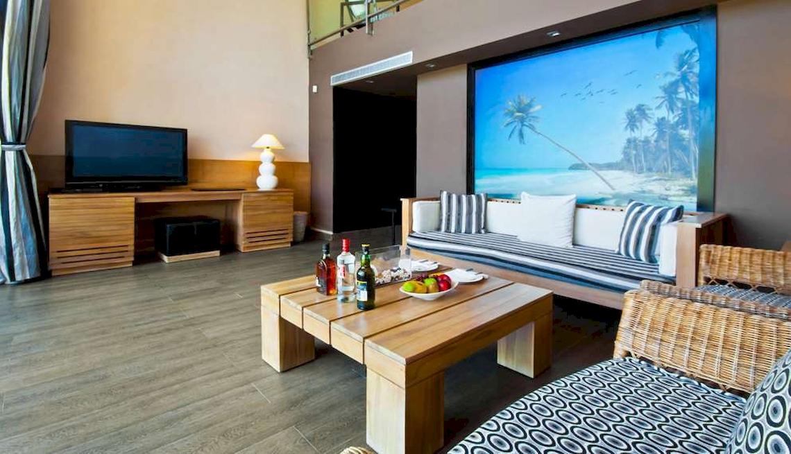 Innenraum des Catalonia Royal Bavaro Hotel mit Wohnzimmermöbeln, Fernseher, Tisch mit Flaschen und Obst.