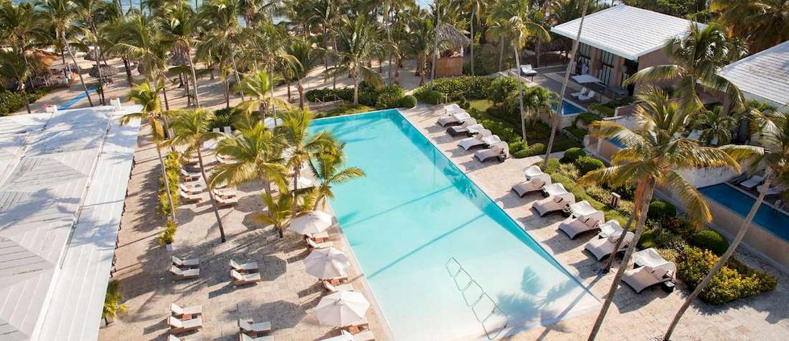 Oberflächenansicht des Catalonia Royal Bavaro Hotels mit Swimmingpool, Liegestühlen und Palmen.