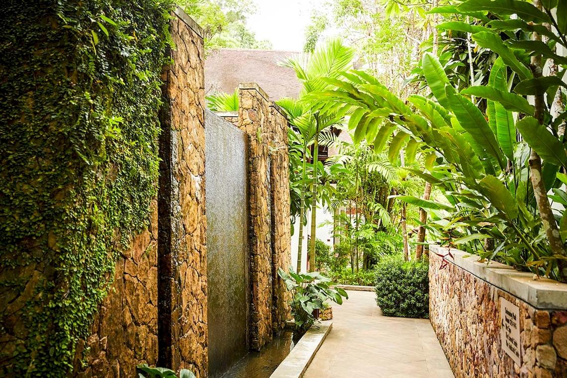 Gartenweg im Tubkaak Krabi Boutique Resort mit Steinmauern und Wasserfall.