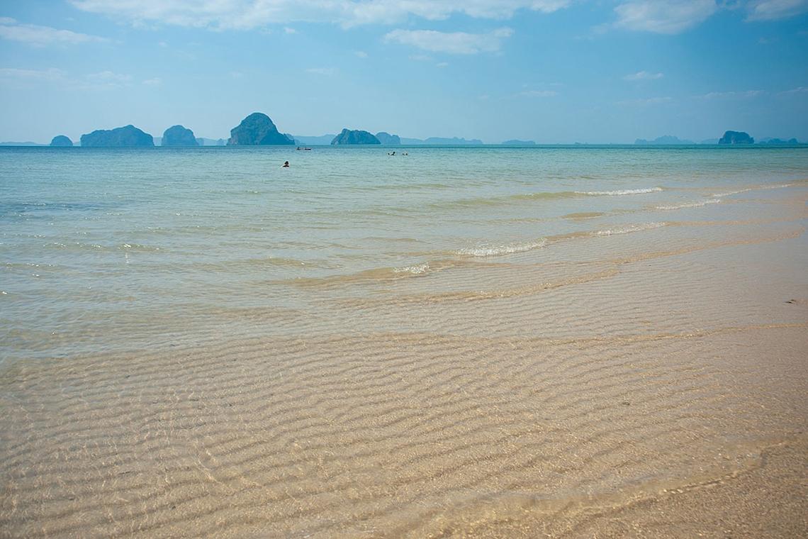 Strand des Tubkaak Krabi Boutique Resorts mit kleinen Wellen im Wasser und Inseln im Hintergrund