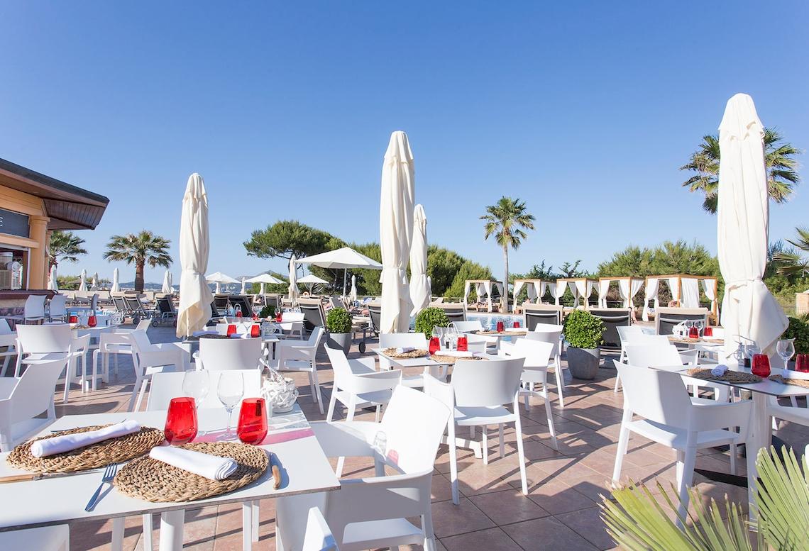 Außenbereich des Sarena de Muro Resort Mallorca mit weißen Tischen und Stühlen unter Schirmen.