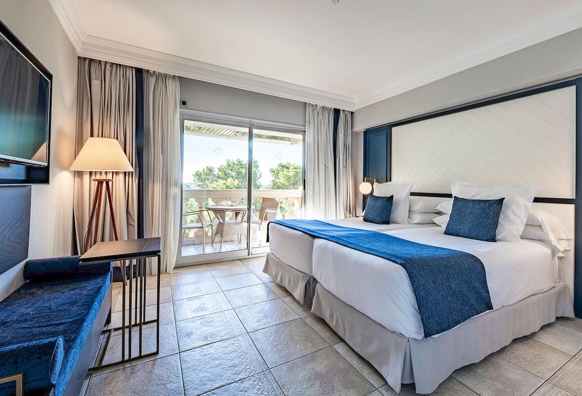 Hotelzimmer im Sarena de Muro Resort Mallorca mit Balkon, zwei Betten, Fernseher und Lampe.
