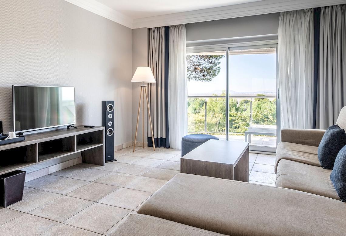Wohnzimmer mit Fernseher, Lautsprechern, Couch und Fenstern im Sarena de Muro Resort Mallorca