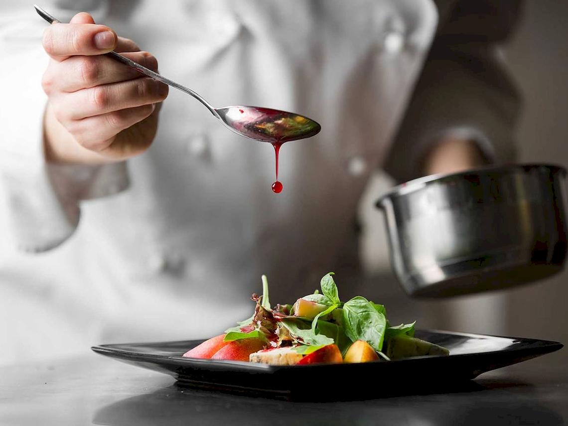 Koch tropft rote Sauce auf ein Salatgericht auf einem schwarzen Teller