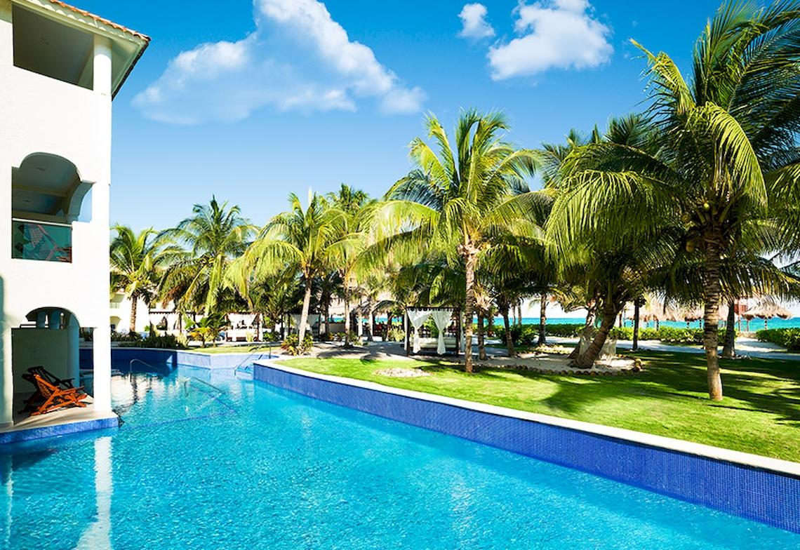 Außenpool des El Dorado Royale Spa Resort mit Palmen und Meer im Hintergrund