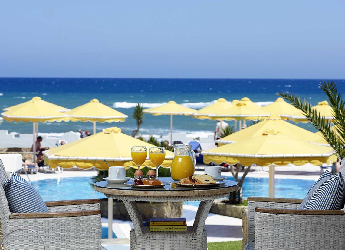 Frühstück am Pool im Serita Beach Hotel mit gelben Sonnenschirmen und Blick auf das Meer.