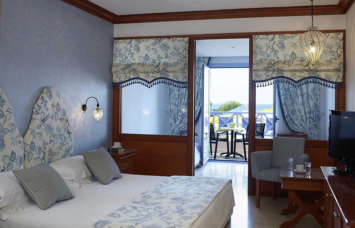 Innenansicht eines Zimmers im Serita Beach Hotel mit Blick auf einen Balkon und Meer.
