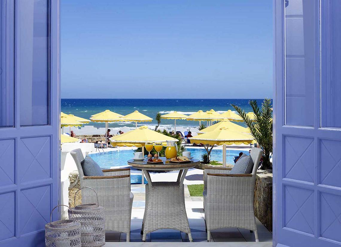 Aussicht von der Terrasse des Serita Beach Hotels auf das Meer und den Poolbereich mit gelben Sonnenschirmen.