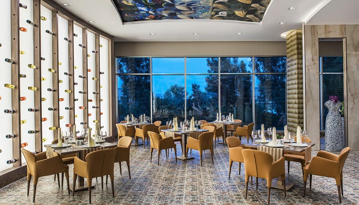 Innenraum des Delphin BE Grand Resort Restaurants mit großen Fenstern und modernen Möbeln.