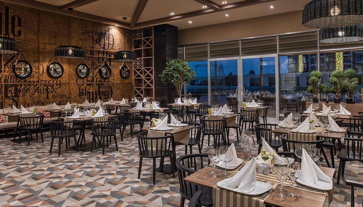 Innenansicht des Restaurants im Delphin BE Grand Resort mit geometrischen Bodenfliesen und gedeckten Tischen.