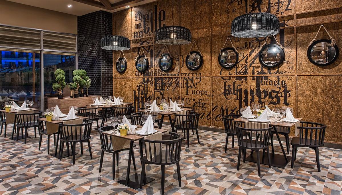 Innenansicht des Restaurants im Delphin BE Grand Resort mit runden Spiegeln und geometrischem Bodenbelag.