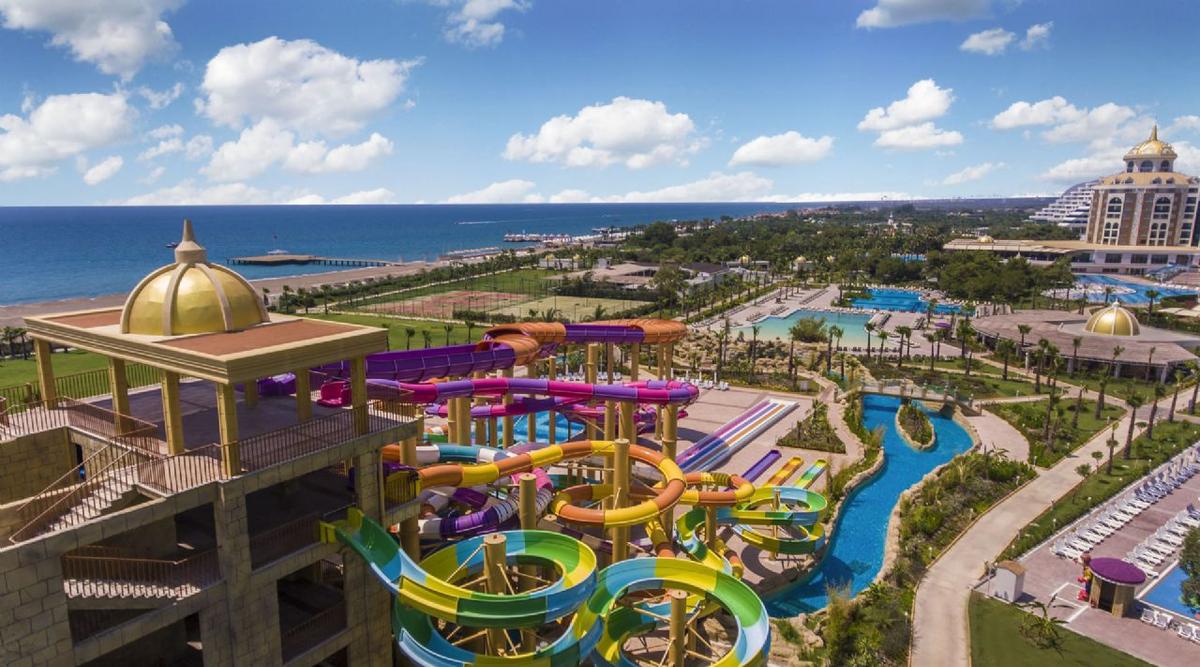Luftaufnahme des Delphin BE Grand Resort Wasserparks mit bunten Rutschen und Blick auf das Meer