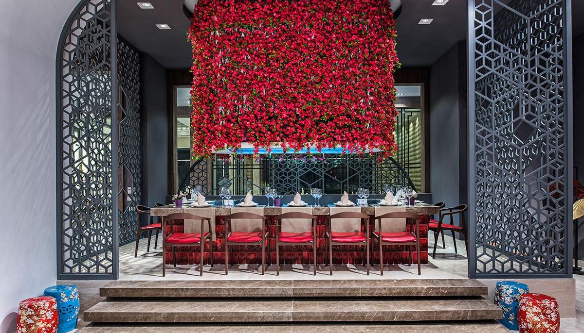 Ein eleganter Essbereich im Delphin BE Grand Resort mit einem Tisch voller Gläser und Tellern, umgeben von roten Blumen.