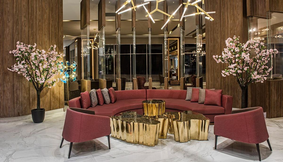 Lobby im Delphin BE Grand Resort mit rotem Sofa, goldenen Tischen und rosa Sträuchern.