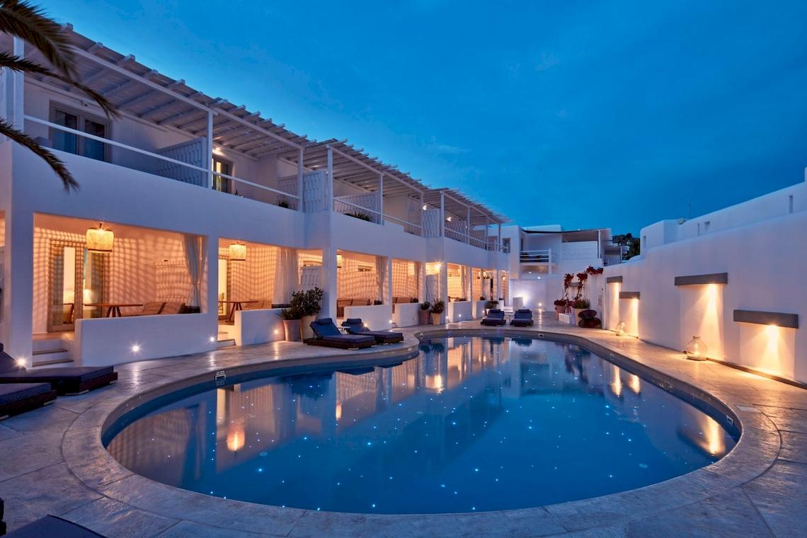 Nachtansicht des Mykonos Ammos Hotels mit beleuchtetem Pool und Loungebereich.
