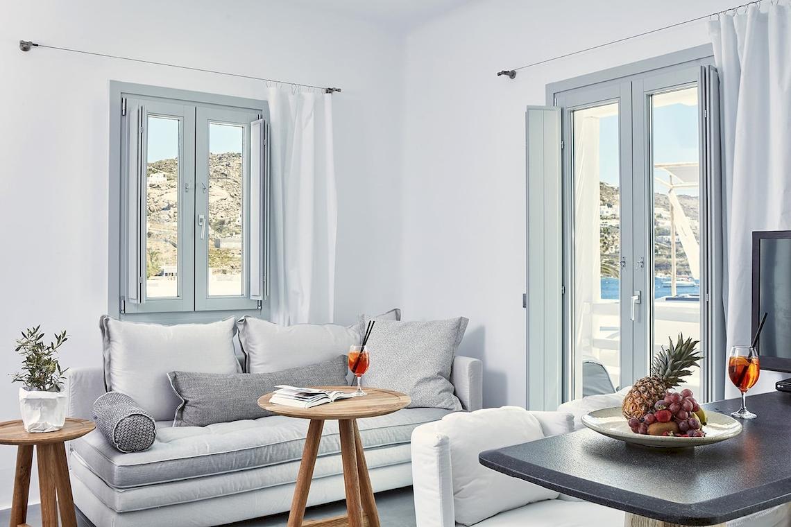 Innenansicht des Wohnzimmers im Mykonos Ammos Hotel mit Couch, Tisch und Ausblick aufs Meer.