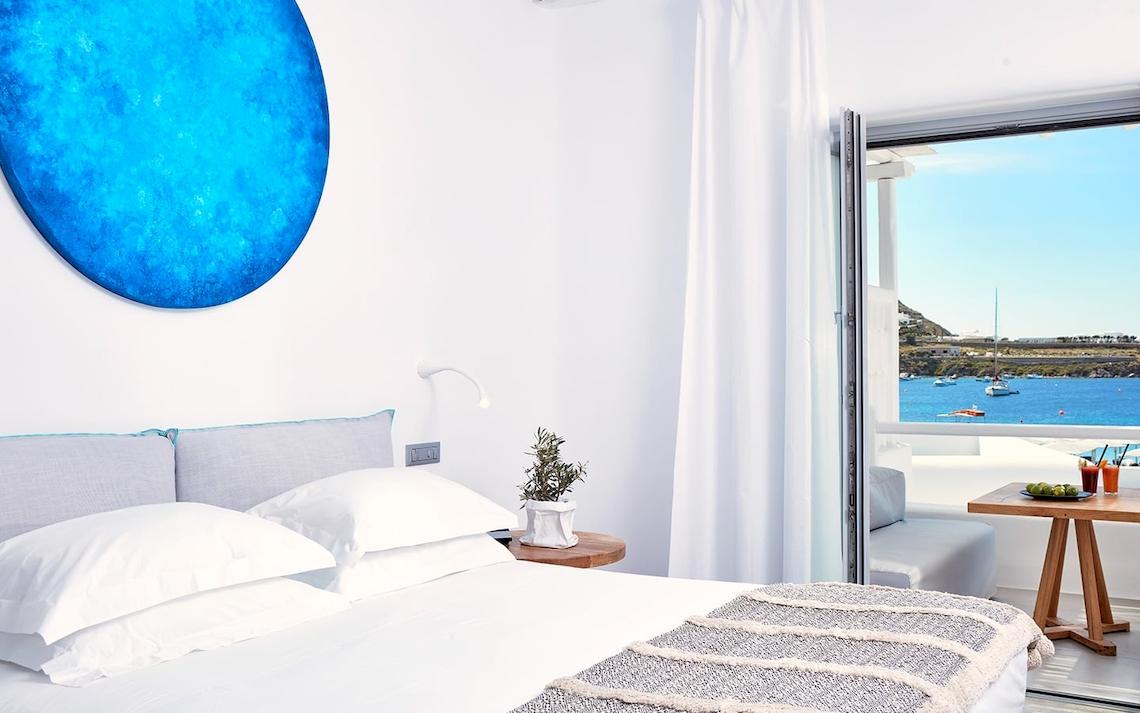 Innenansicht eines Zimmers im Mykonos Ammos Hotel mit Bett, Kissen und Meerblick.