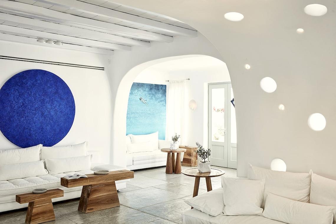 Innenraum des Mykonos Ammos Hotels mit weißen Möbeln, blauem Wandbild und offenem Fenster.