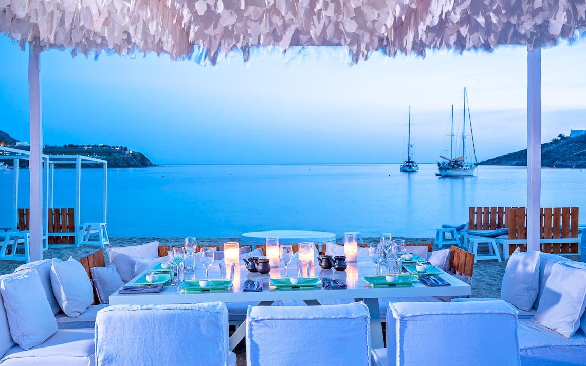 Restauranttisch im Mykonos Ammos mit Blick aufs Meer und zwei Segelboote im Hintergrund.